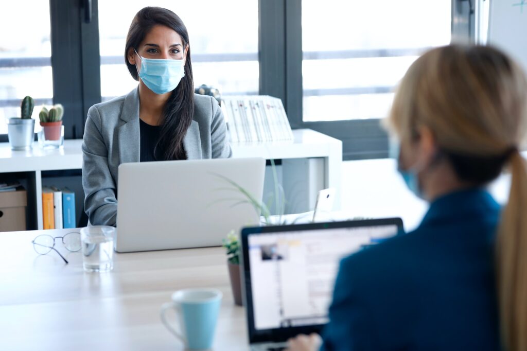 businesswomen wearing a hygienic face mask while working with laptops in the coworking space nearby